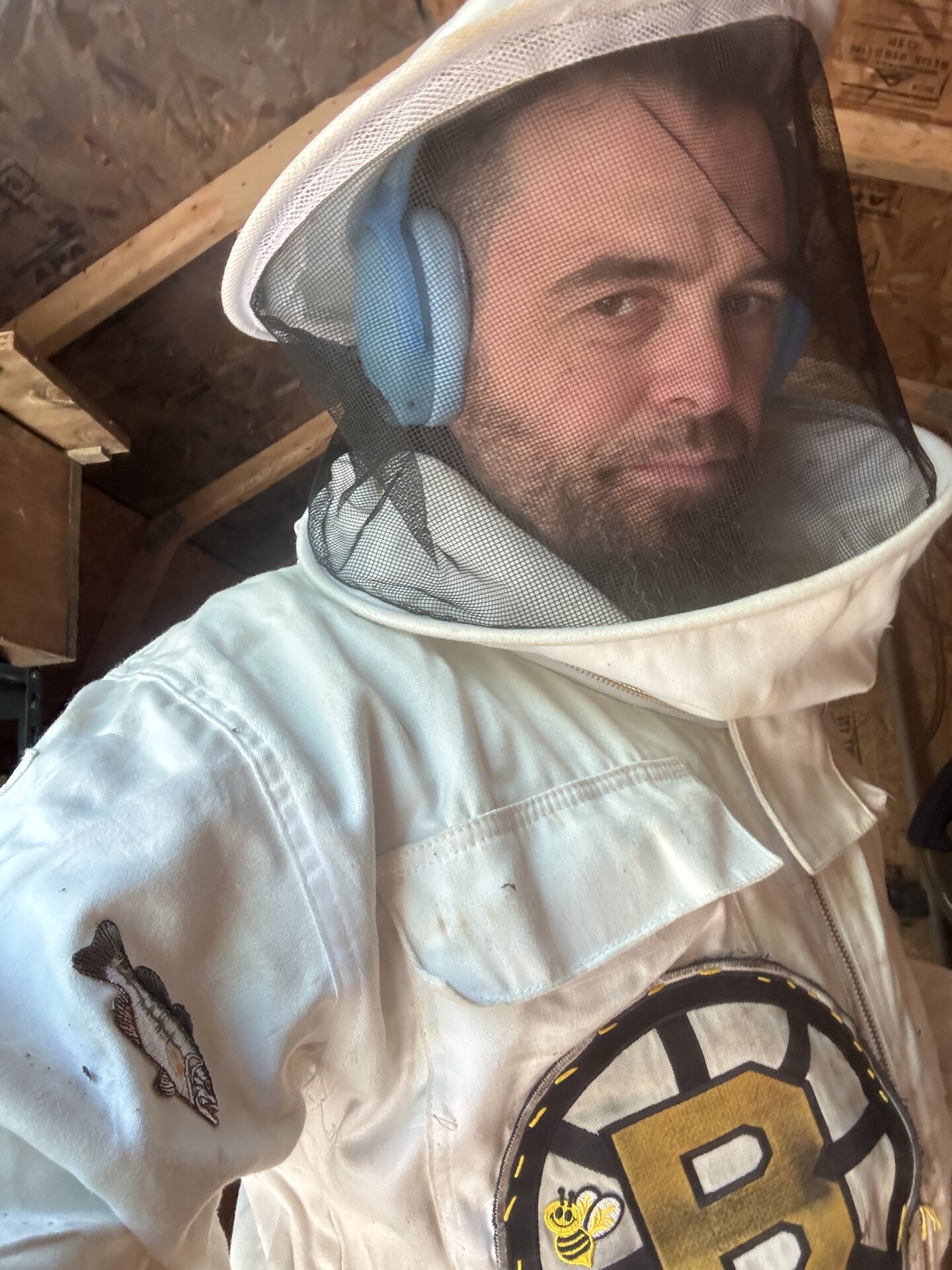 Selfie inside a beekeeping veil. White suit with a Bruins B logo and a bee in the middle on the chest, fish patch on the sleeve.
