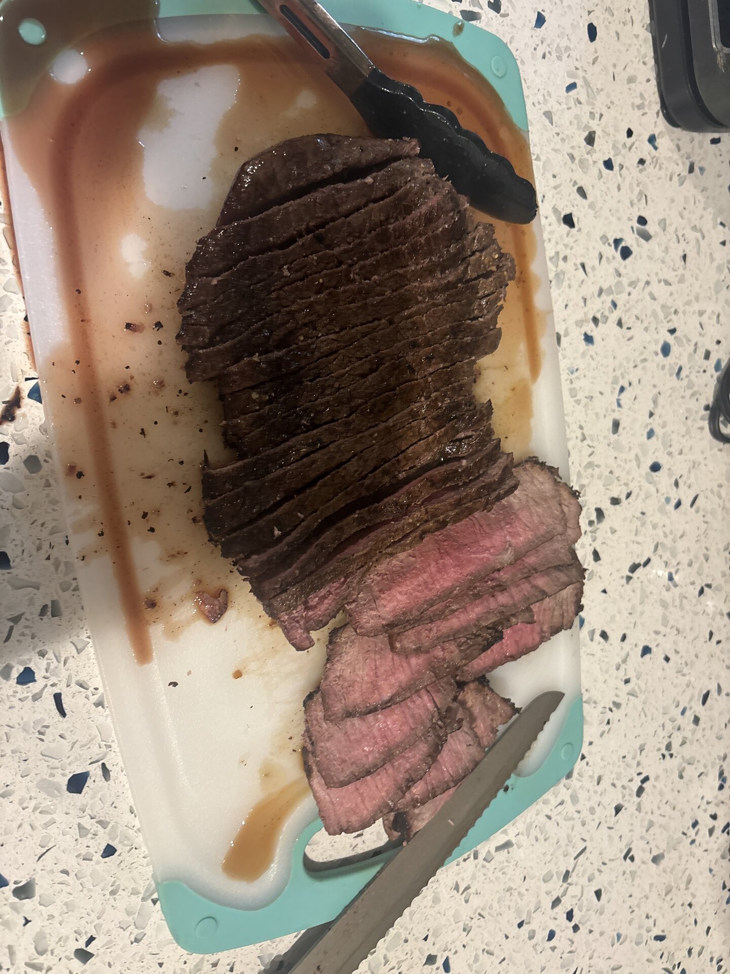 sliced london broil on cutting board — dark crust, pink center